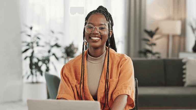 Oranssipaitainen nainen katsoo hymyillen kameraan